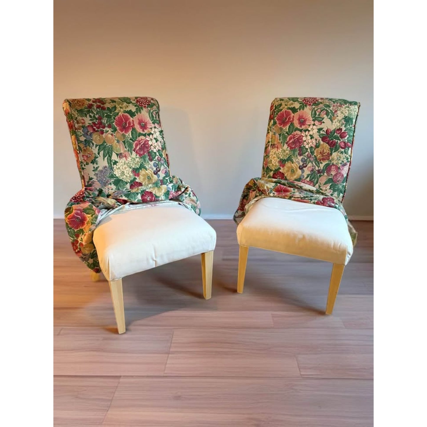 Pair of white upholstered chairs with floral covers over them